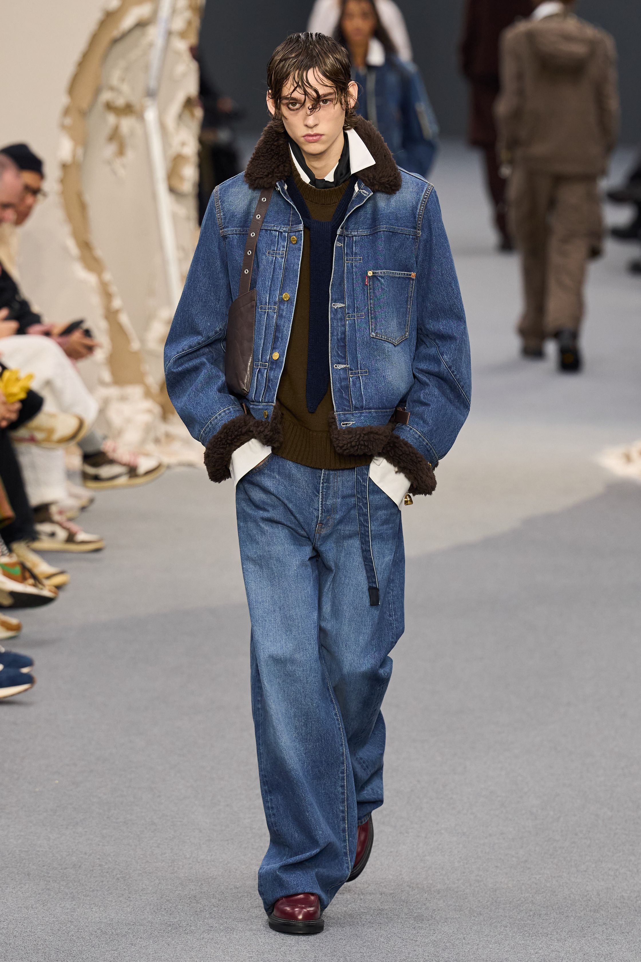 Sacai 2026秋冬再次展示其无可复制的“混合美学”。正装、牛仔、皮草与制服元素被高度结构化地拼接，形成既熟悉又陌生的服装形态。性别边界被进一步模糊，层叠结构制造流动节奏，使行走本身成为设计的一部分。系列在秩序与混乱之间找到平衡，是Sacai 对当代复杂生活状态的持续回应-顽石频道趋势研究